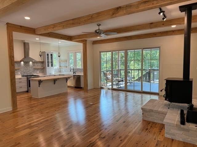 living room featuring beam ceiling, light hardwood / wood-style floors, a healthy amount of sunlight, and a wood stove