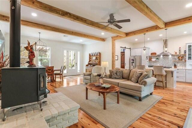 living room with beamed ceiling, a barn door, light hardwood / wood-style flooring, and a wood stove