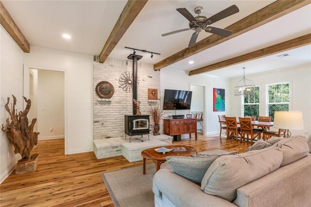 living room with ceiling fan, track lighting, light hardwood / wood-style floors, beamed ceiling, and a wood stove