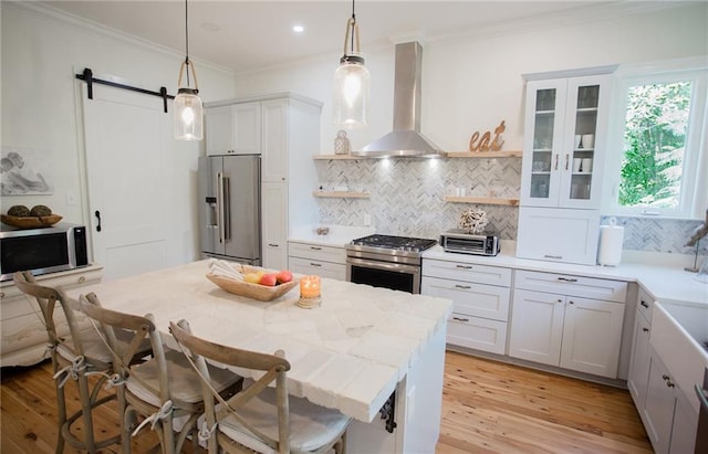 kitchen with a breakfast bar, pendant lighting, stainless steel appliances, a barn door, and wall chimney range hood