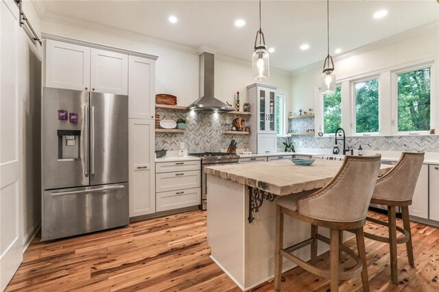 kitchen featuring hanging light fixtures, stainless steel appliances, a center island, a kitchen bar, and wall chimney exhaust hood