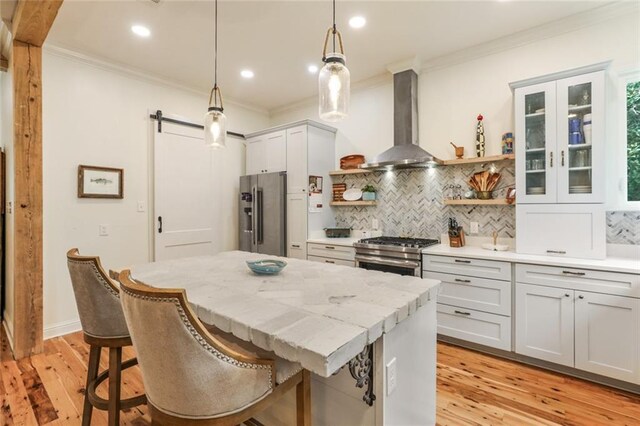 kitchen featuring a kitchen bar, pendant lighting, stainless steel appliances, a barn door, and wall chimney range hood