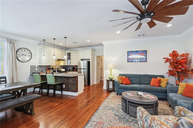 living room featuring hardwood / wood-style flooring, crown molding, sink, and ceiling fan