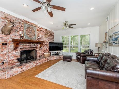 living room with brick wall, a fireplace, hardwood / wood-style floors, and ceiling fan