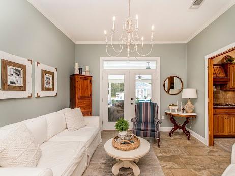 tiled living room with a notable chandelier, crown molding, and french doors