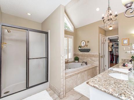 bathroom with tile patterned flooring, lofted ceiling, a chandelier, vanity, and shower with separate bathtub