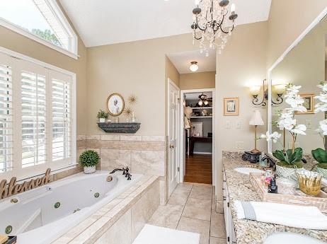 bathroom with a relaxing tiled tub, dual vanity, lofted ceiling, hardwood / wood-style flooring, and a notable chandelier