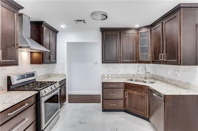 kitchen with light stone counters, stainless steel appliances, wall chimney exhaust hood, decorative backsplash, and sink