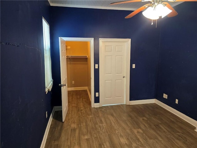 unfurnished bedroom featuring dark wood-style floors, baseboards, and a walk in closet