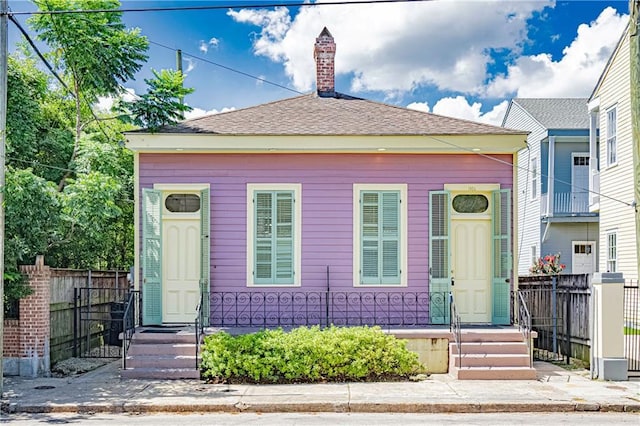 view of front of home featuring fence, roof with shingles, and a chimney