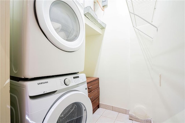 washroom with laundry area, light tile patterned flooring, baseboards, and stacked washer and clothes dryer