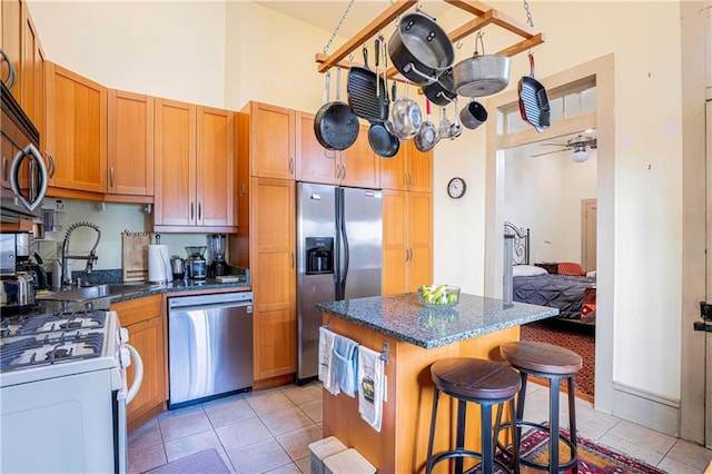 kitchen with ceiling fan, a high ceiling, stainless steel appliances, a kitchen island, and light tile patterned floors