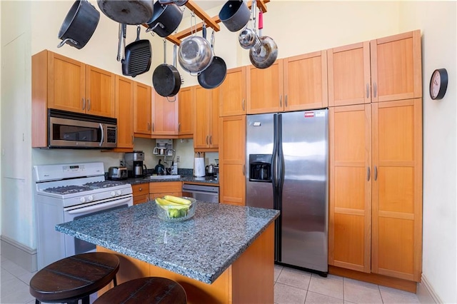 kitchen with light tile patterned floors, dark stone counters, stainless steel appliances, a kitchen breakfast bar, and a center island