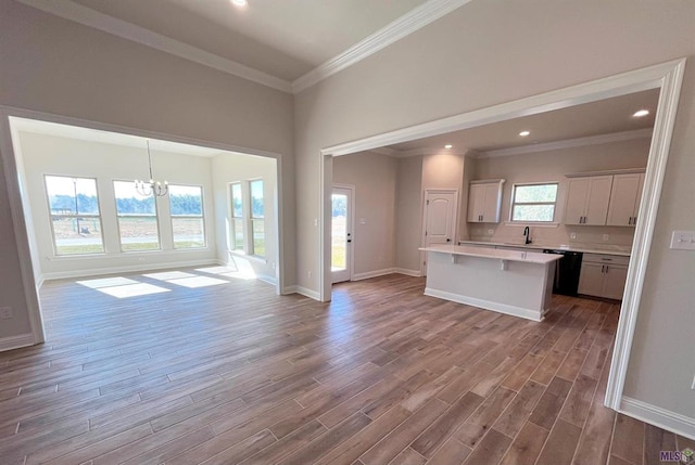 unfurnished living room with sink, hardwood / wood-style floors, crown molding, and an inviting chandelier