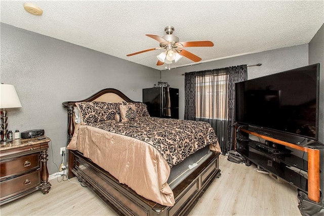 bedroom featuring black fridge, light hardwood / wood-style flooring, a textured ceiling, and ceiling fan