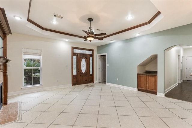 tiled foyer entrance with ceiling fan, ornamental molding, and a raised ceiling