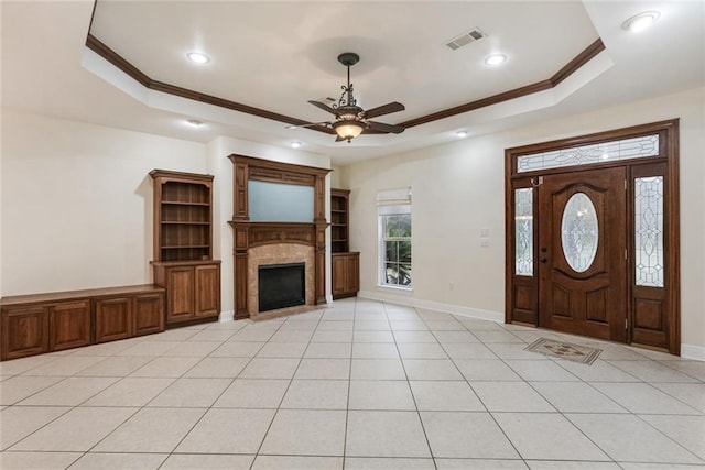 tiled entryway with a raised ceiling, ornamental molding, ceiling fan, and a fireplace