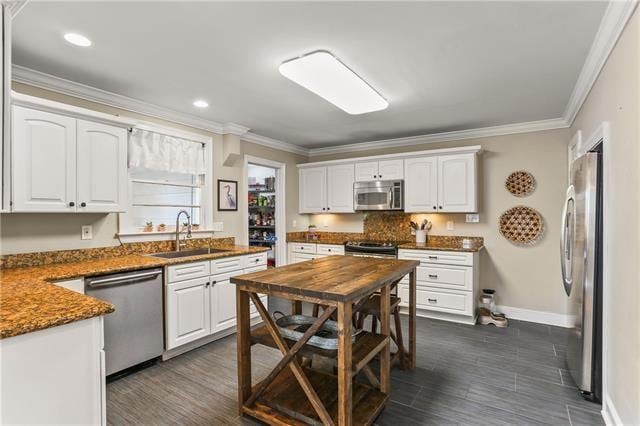 kitchen featuring white cabinets, ornamental molding, sink, dark stone countertops, and appliances with stainless steel finishes