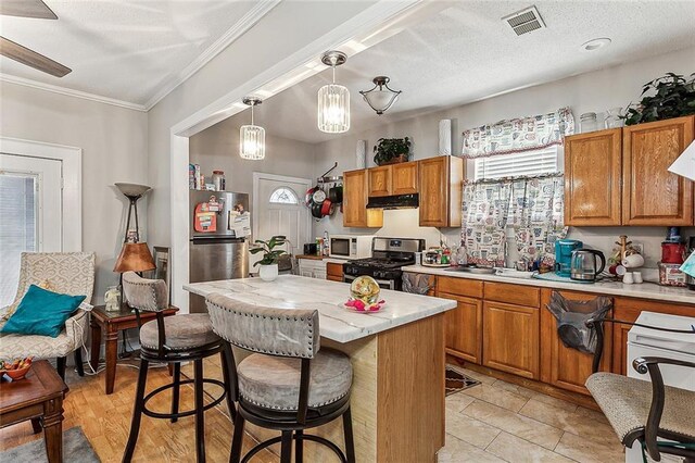 kitchen featuring stainless steel appliances, pendant lighting, a kitchen island, crown molding, and light wood-type flooring