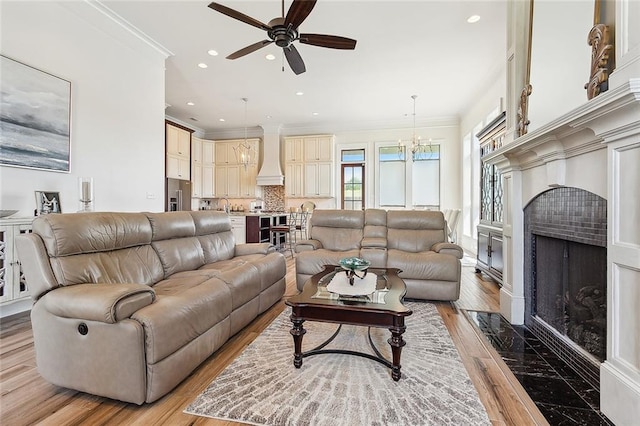 living room featuring ceiling fan with notable chandelier, light hardwood / wood-style floors, sink, and ornamental molding