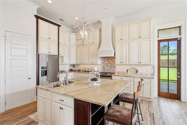 kitchen featuring custom range hood, an island with sink, stainless steel appliances, light hardwood / wood-style floors, and light stone countertops