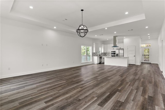 unfurnished living room with a tray ceiling, a notable chandelier, and dark hardwood / wood-style flooring