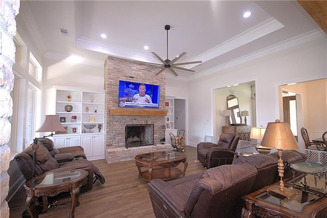 living room featuring ceiling fan, light wood-type flooring, brick wall, a raised ceiling, and a brick fireplace