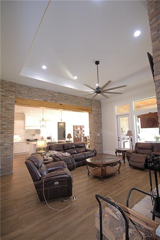 living room featuring ceiling fan with notable chandelier, a raised ceiling, and hardwood / wood-style floors