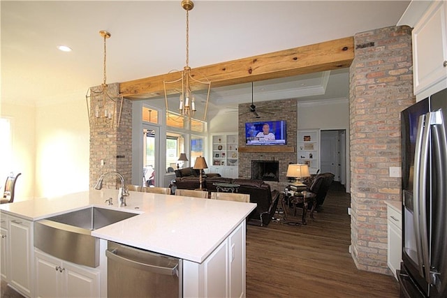 kitchen with stainless steel appliances, white cabinetry, a brick fireplace, brick wall, and dark wood-type flooring