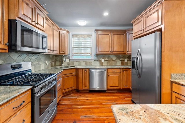 kitchen featuring tasteful backsplash, stainless steel appliances, sink, light stone counters, and wood-type flooring