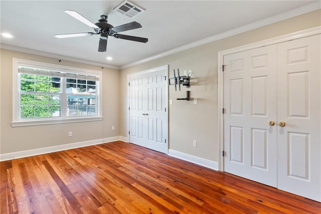 unfurnished bedroom with two closets, ceiling fan, hardwood / wood-style flooring, and ornamental molding