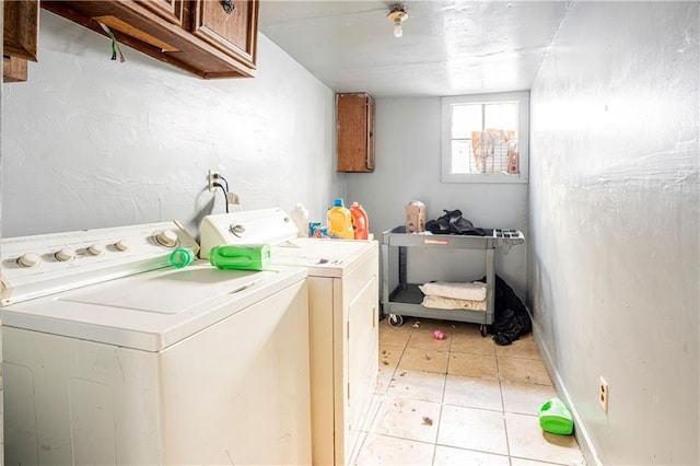 clothes washing area featuring cabinets, light tile patterned floors, and washing machine and clothes dryer