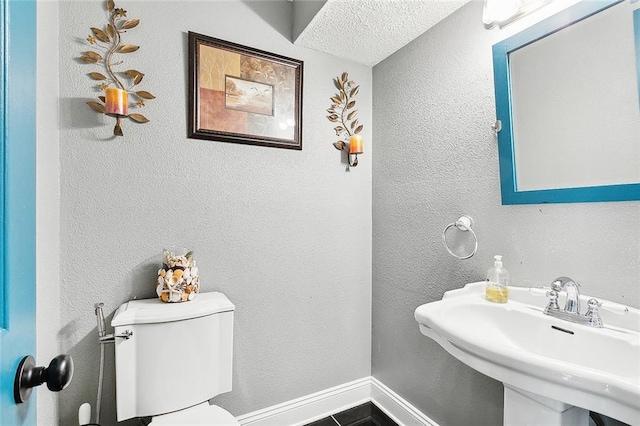 bathroom with a textured ceiling, toilet, sink, and tile patterned flooring