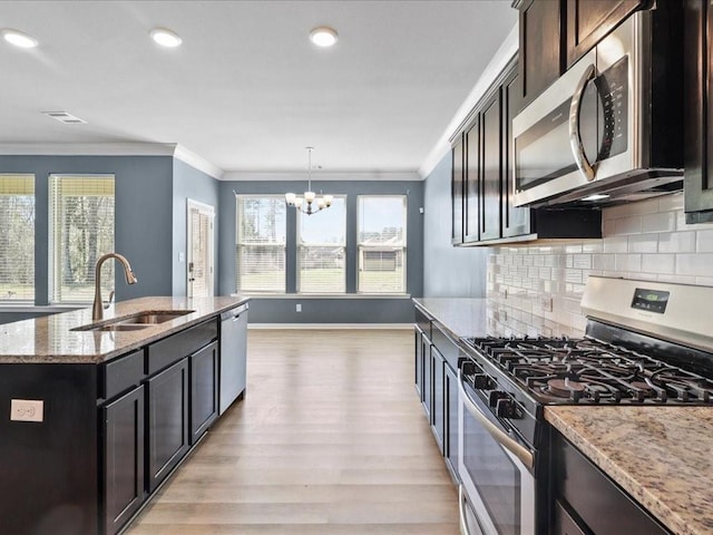 kitchen with light wood-type flooring, an island with sink, sink, light stone countertops, and appliances with stainless steel finishes