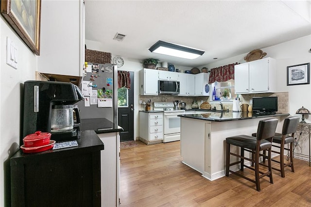 kitchen featuring electric stove, white cabinets, light wood-type flooring, kitchen peninsula, and backsplash