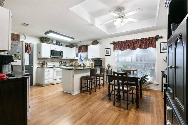 kitchen featuring white cabinets, a breakfast bar, white range with electric cooktop, light hardwood / wood-style floors, and a tray ceiling