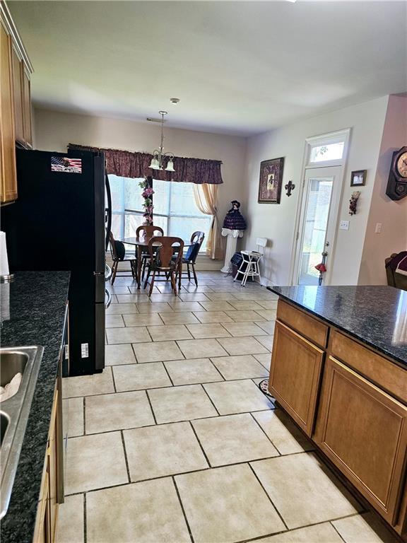 669 Lake Iberville Ct, Ponchatoula, LA 70454 - kitchen with brown cabinets, freestanding refrigerator, light tile patterned flooring, dark stone counters, and a sink