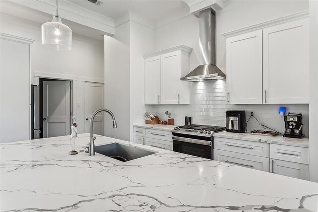 kitchen with gas stove, wall chimney exhaust hood, decorative backsplash, pendant lighting, and sink