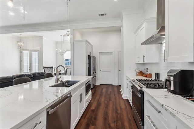 kitchen with dark wood-type flooring, stainless steel appliances, wall chimney exhaust hood, decorative light fixtures, and sink