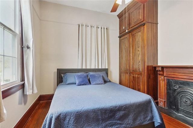 bedroom with dark hardwood / wood-style flooring, a premium fireplace, and ceiling fan