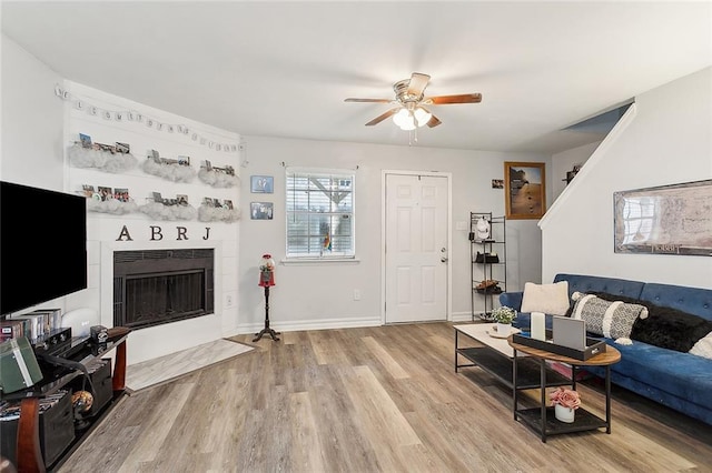 living room with a tiled fireplace, light hardwood / wood-style flooring, and ceiling fan