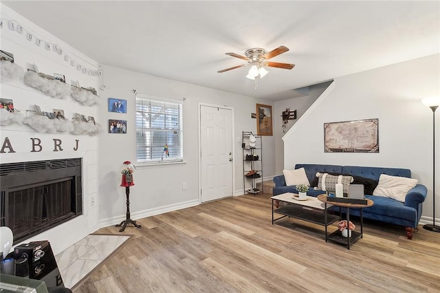 living room featuring a tile fireplace, light wood-type flooring, and ceiling fan