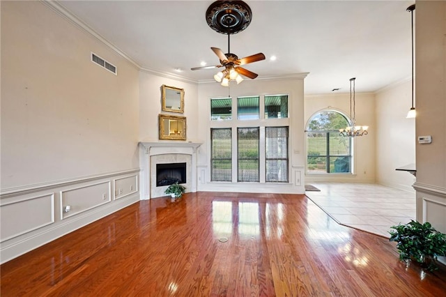 unfurnished living room with a tiled fireplace, ceiling fan with notable chandelier, crown molding, and light hardwood / wood-style floors