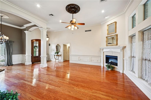 unfurnished living room featuring wood-type flooring, ceiling fan with notable chandelier, ornamental molding, and a tile fireplace