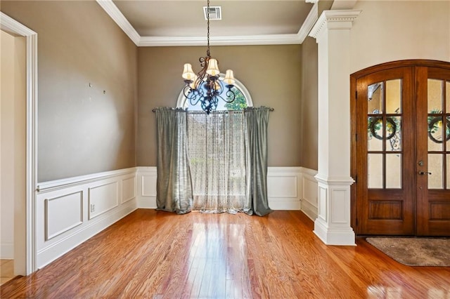 unfurnished dining area featuring crown molding, light wood-type flooring, a chandelier, and ornate columns