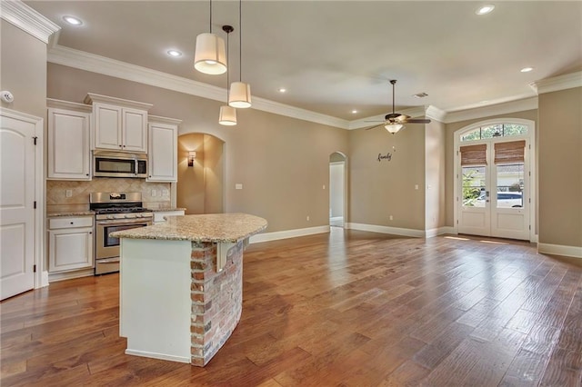 kitchen with appliances with stainless steel finishes, light stone countertops, backsplash, white cabinetry, and hardwood / wood-style flooring