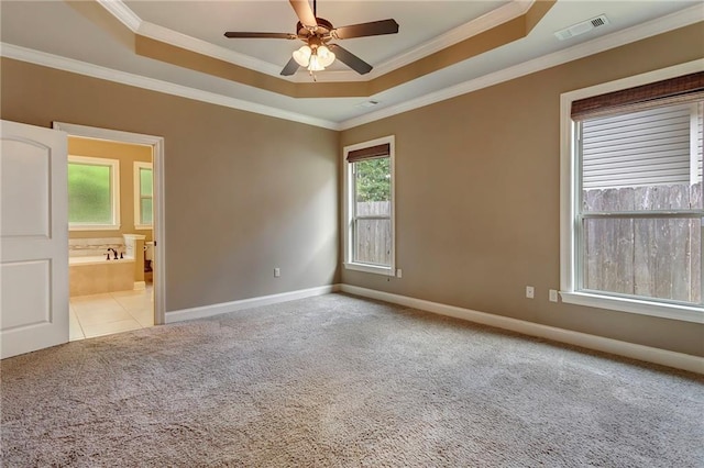 empty room with visible vents, light colored carpet, a ceiling fan, crown molding, and a raised ceiling
