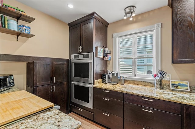 kitchen with dark brown cabinetry, double oven, and light stone countertops