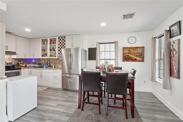 kitchen with white cabinets, light wood-type flooring, stainless steel appliances, and backsplash