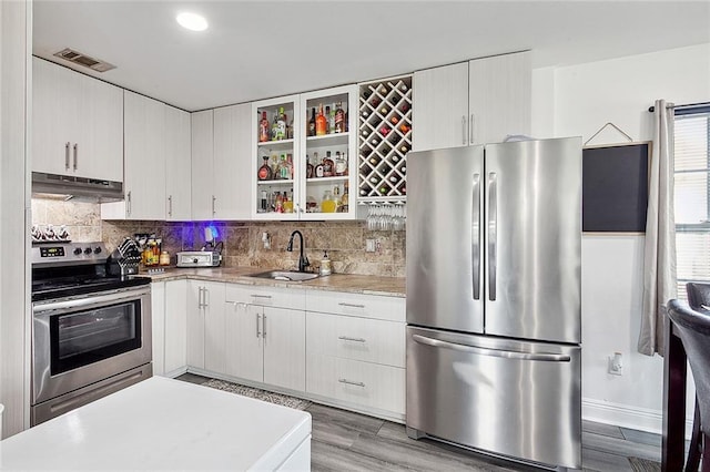 kitchen with light hardwood / wood-style flooring, stainless steel appliances, white cabinets, tasteful backsplash, and sink